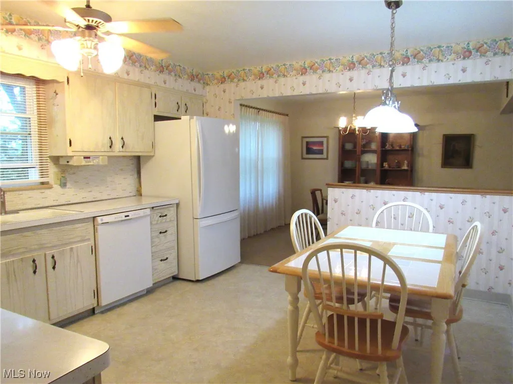 Kitchen featuring wallpapered walls, light countertops, white appliances, pendant lighting, and light brown cabinets