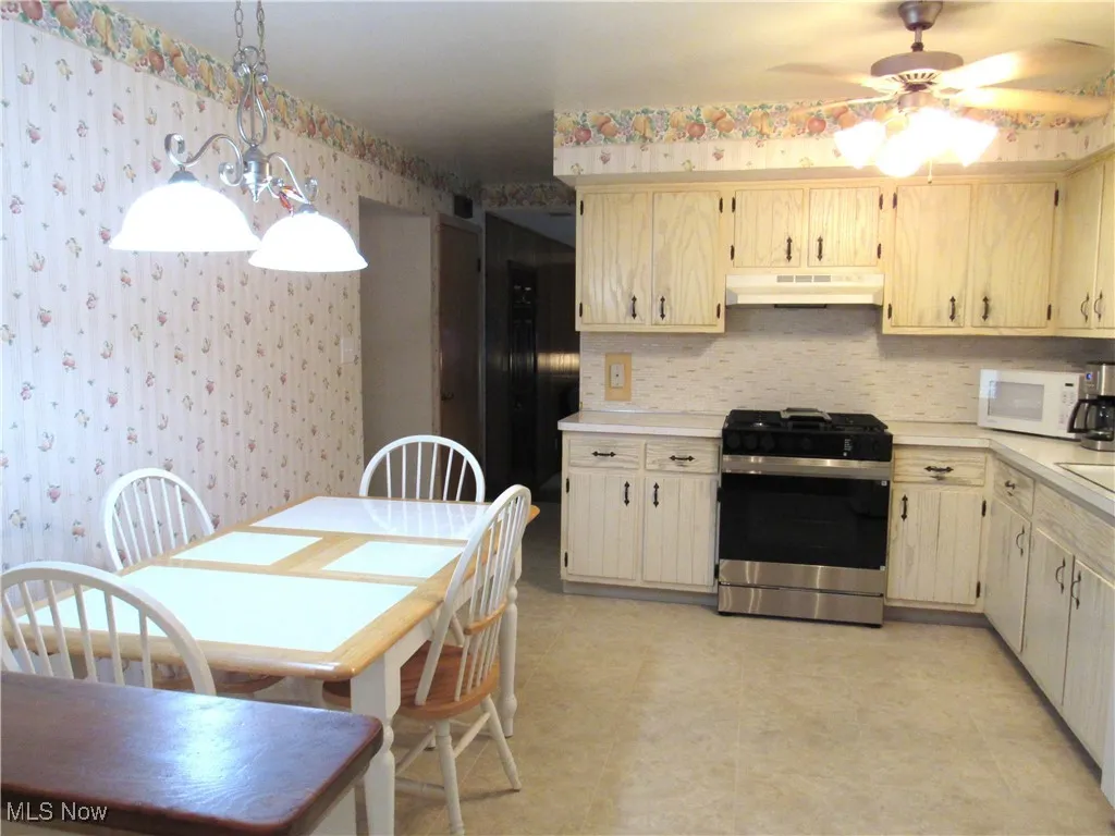 Kitchen with stainless steel gas range, light countertops, decorative light fixtures, white microwave, and under cabinet range hood