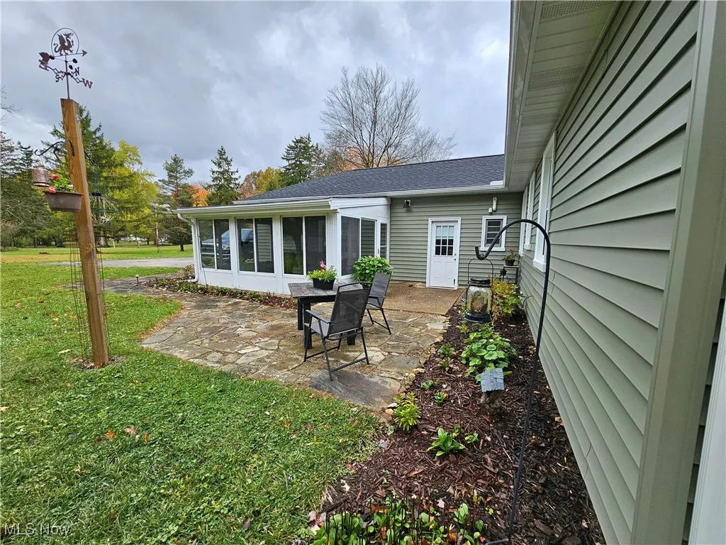 Rear view of house featuring a sunroom, a patio area, a lawn, and a shingled roof