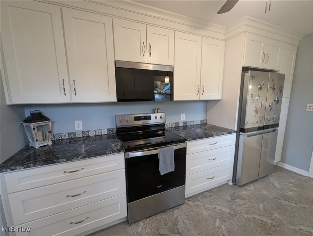 Kitchen featuring stainless steel appliances, white cabinetry, dark stone counters, and a ceiling fan