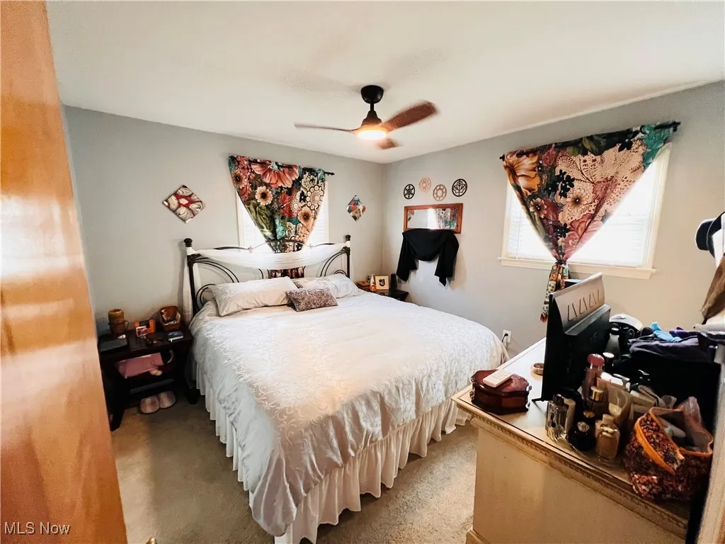 Bedroom featuring light colored carpet, multiple windows, and a ceiling fan