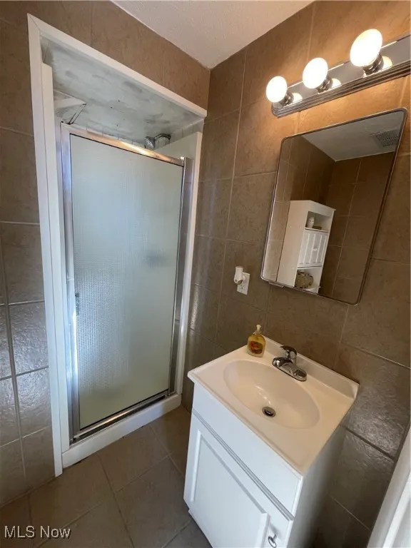 Full bathroom featuring tile walls, light tile patterned floors, vanity, a shower stall, and a textured ceiling