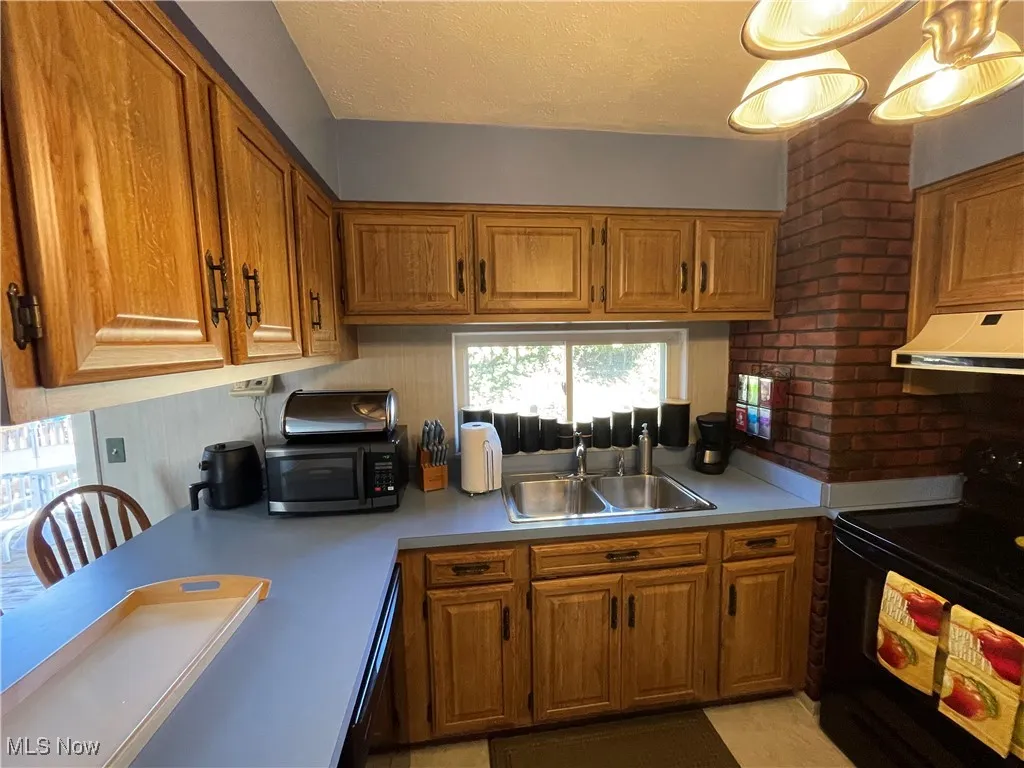 Kitchen with black appliances, brown cabinetry, a textured ceiling, under cabinet range hood, and light countertops