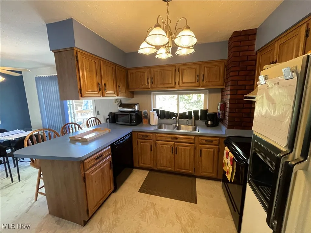 Kitchen featuring a breakfast bar area, a peninsula, black appliances, brown cabinets, and hanging light fixtures