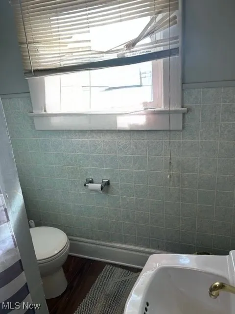 Bathroom with dark wood-style flooring, tile walls, and a wainscoted wall