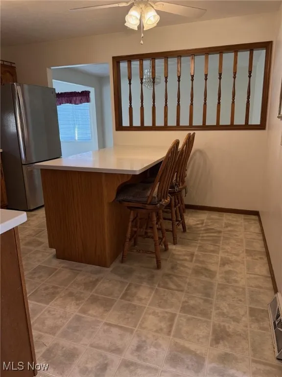 Kitchen with freestanding refrigerator, light countertops, a ceiling fan, brown cabinetry, and a peninsula