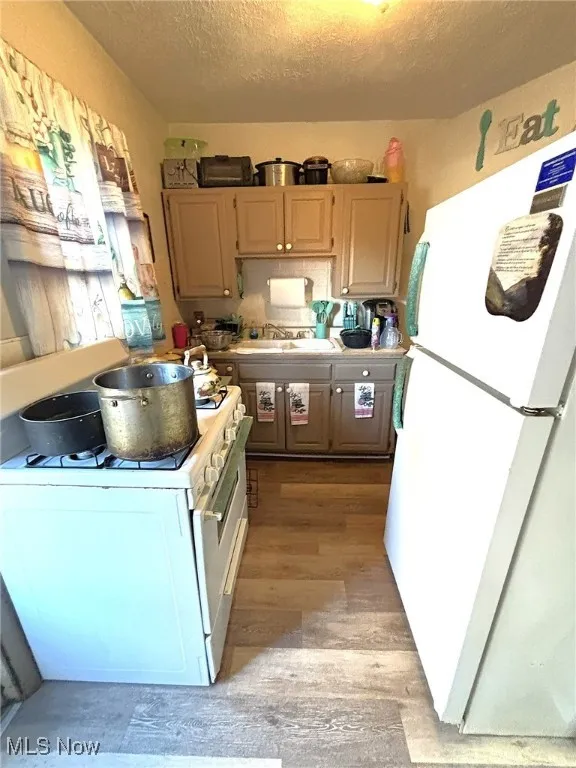 Kitchen with white appliances, light countertops, light wood-style floors, and a textured ceiling