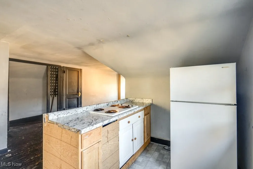 Kitchen featuring white appliances, light countertops, a peninsula, vaulted ceiling, and light brown cabinetry