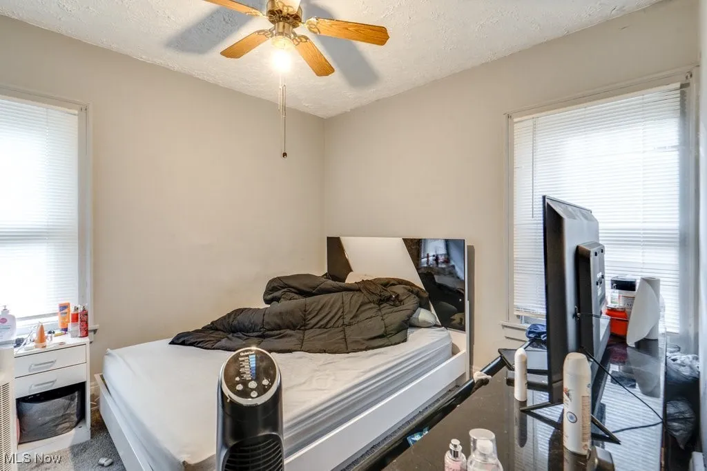 Bedroom featuring a textured ceiling, multiple windows, and a ceiling fan