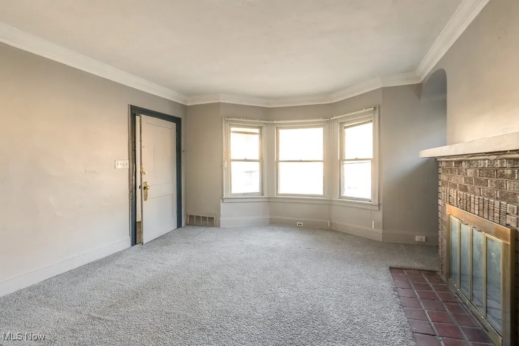 Unfurnished living room featuring crown molding, a fireplace, and carpet floors