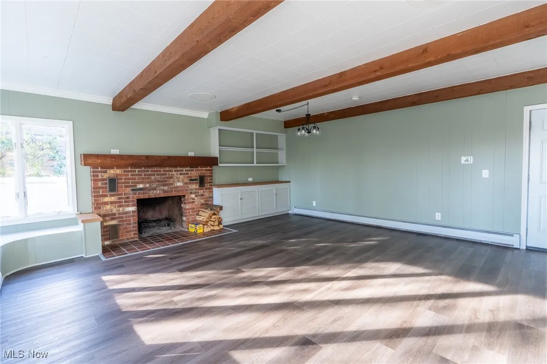 Unfurnished living room featuring a brick fireplace, dark wood-type flooring, a baseboard radiator, beamed ceiling, and wood walls