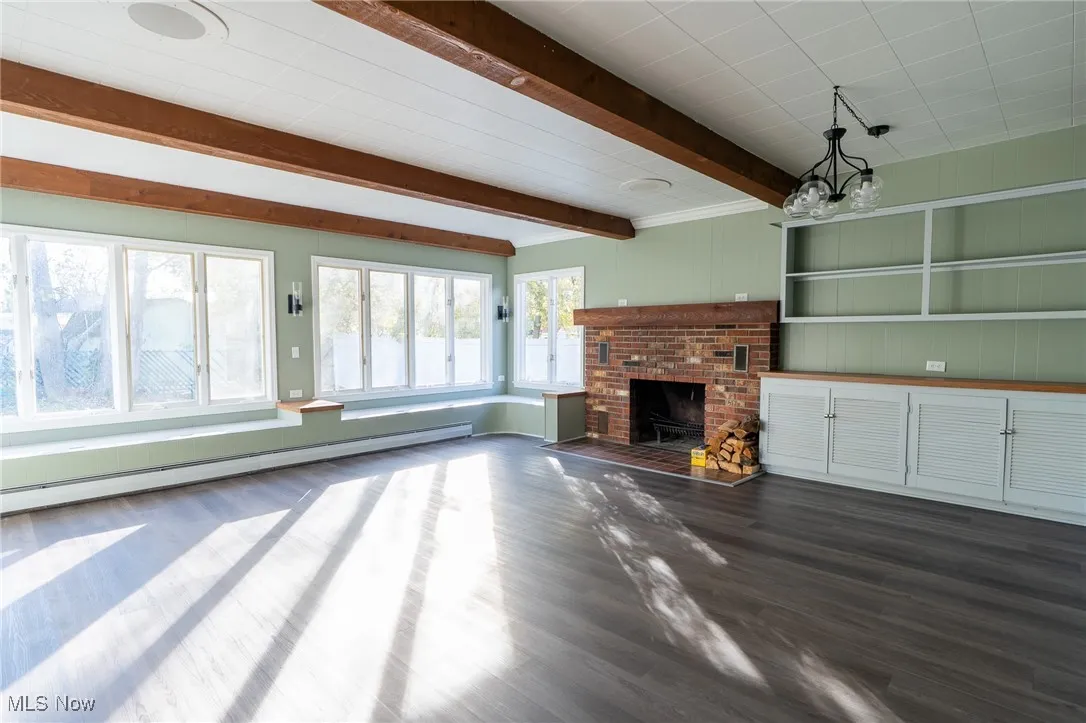 Unfurnished living room with a brick fireplace, dark wood finished floors, baseboard heating, and beam ceiling