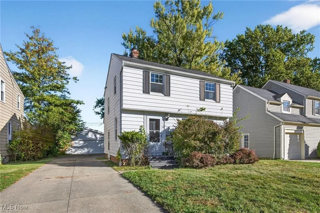 Colonial-style house featuring a garage, an outdoor structure, a chimney, and a front lawn