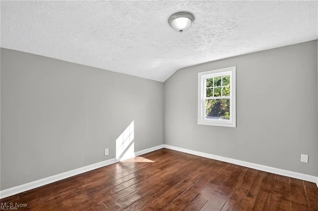 Bonus room with dark wood-style floors, a textured ceiling, and lofted ceiling