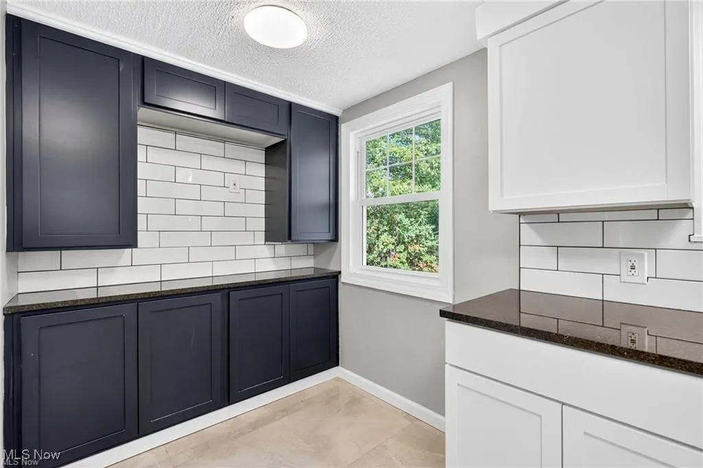 Kitchen with decorative backsplash, dark stone counters, a textured ceiling, and light tile patterned flooring