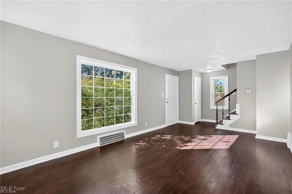 Unfurnished living room featuring a textured ceiling, dark wood finished floors, and stairs