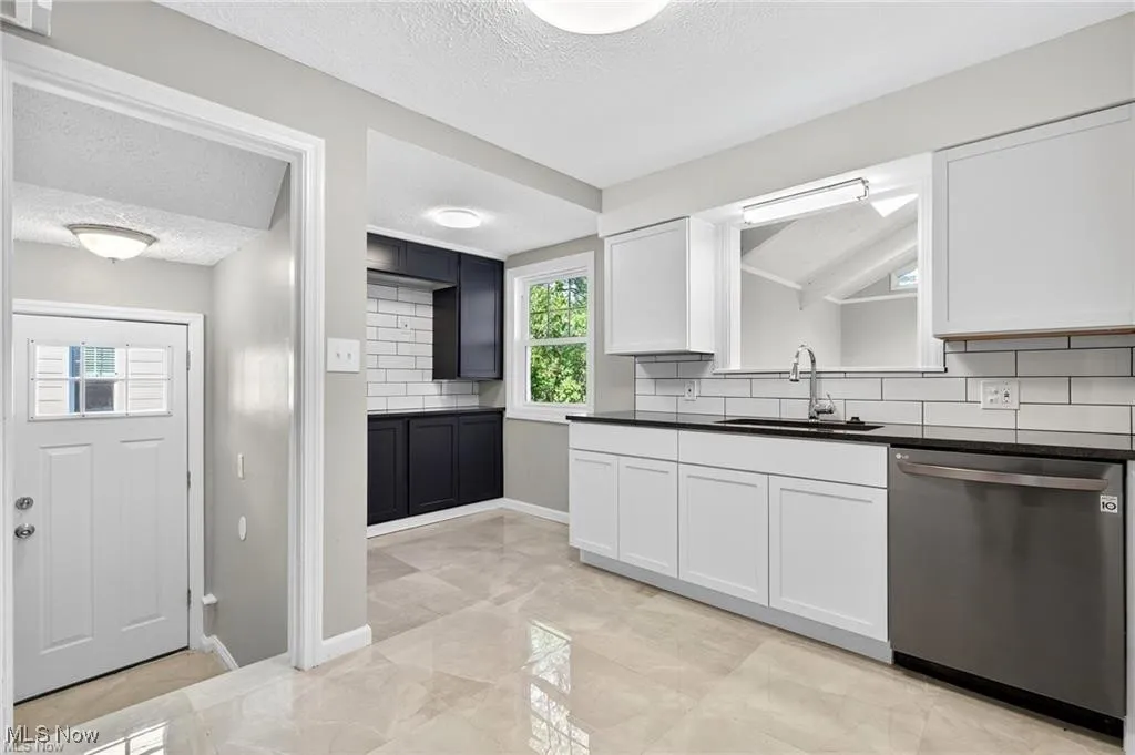 Kitchen featuring backsplash, a textured ceiling, stainless steel dishwasher, and white cabinets
