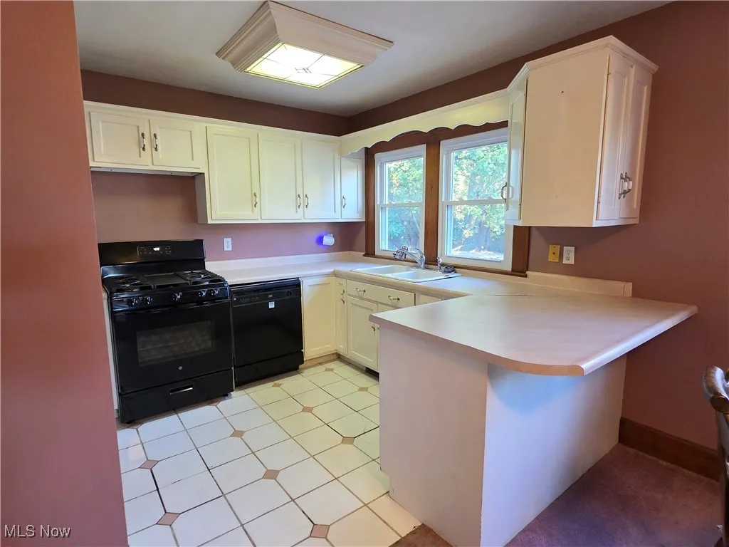 Kitchen featuring black appliances, a peninsula, light countertops, white cabinets, and light tile patterned floors