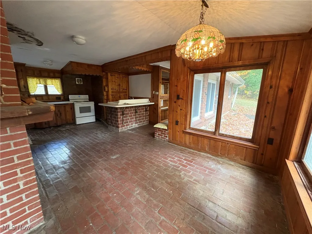 Kitchen featuring wood walls, brick floors, white electric range, light countertops, and a chandelier