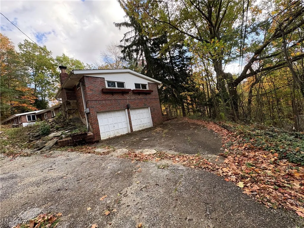 View of side of property featuring brick siding, a chimney, driveway, and an attached garage