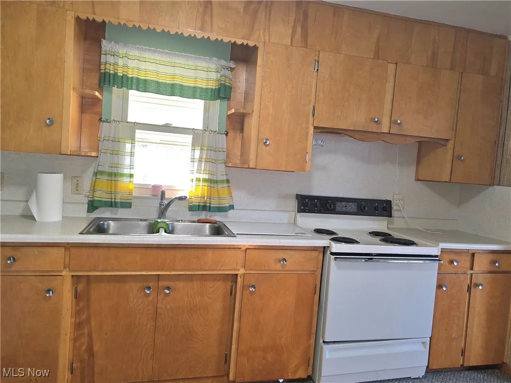 Kitchen with white electric range, light countertops, and brown cabinets