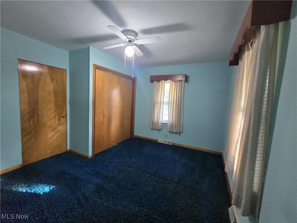 Unfurnished bedroom featuring dark colored carpet, a closet, and ceiling fan