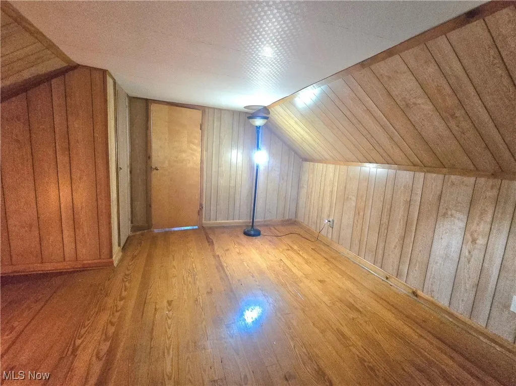 Bonus room featuring lofted ceiling, wooden walls, and wood finished floors
