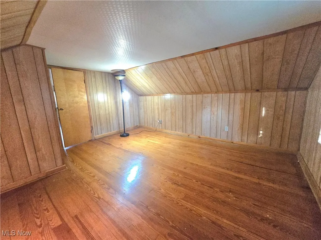 Bonus room featuring wood walls, lofted ceiling, and wood finished floors