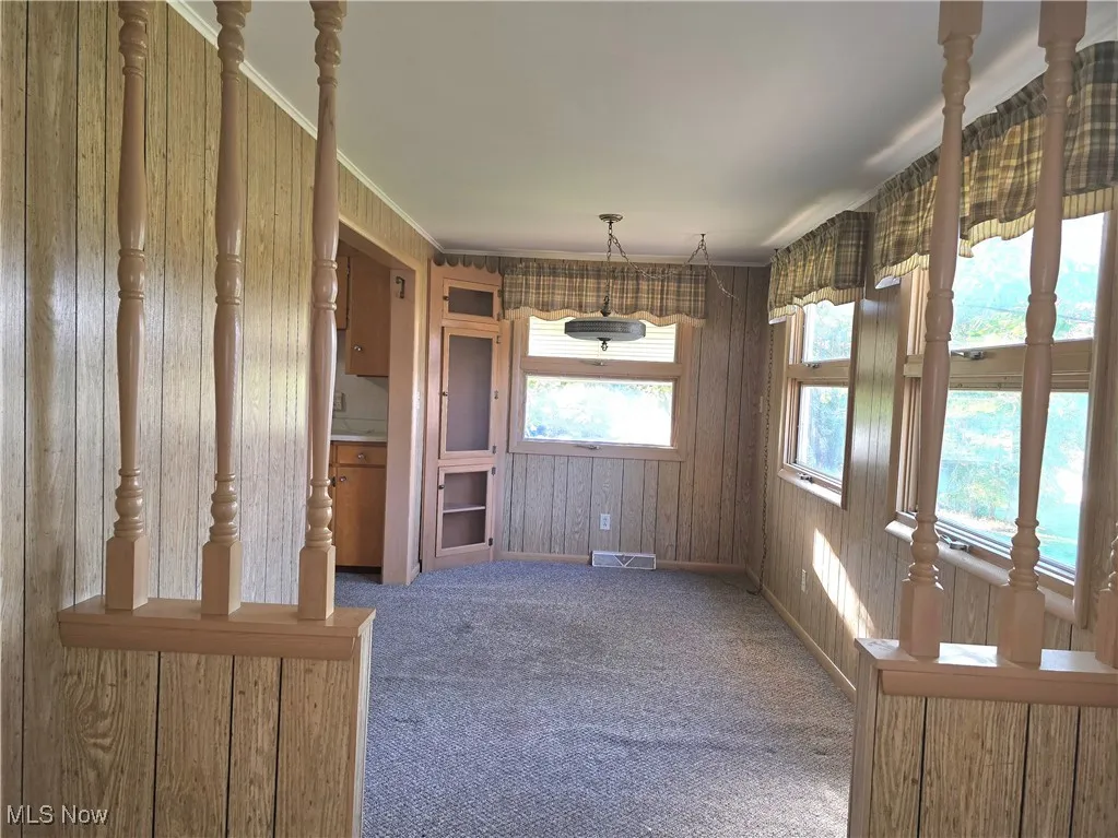 Unfurnished dining area with carpet flooring, crown molding, and wood walls