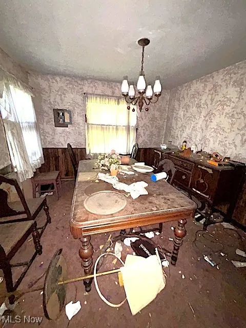 Dining space featuring wainscoting, wallpapered walls, a textured ceiling, a chandelier, and wooden walls