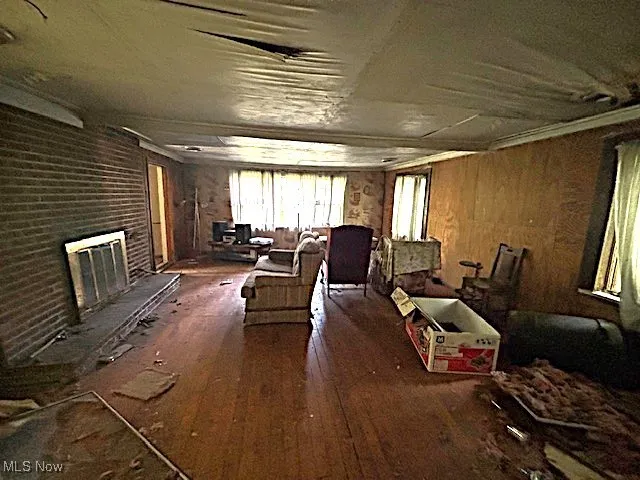 Living area featuring dark wood-style flooring, wood walls, and a brick fireplace