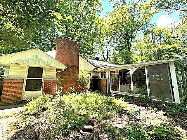View of front of property with brick siding, a chimney, a sunroom, and board and batten siding