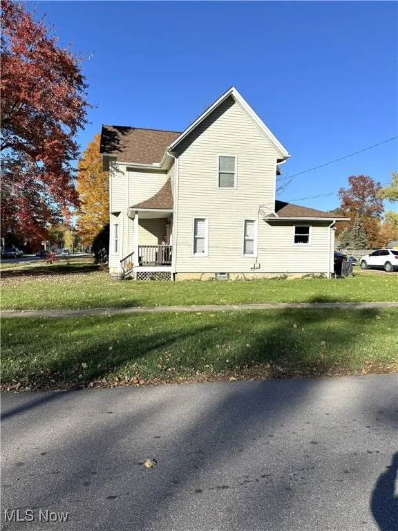 View of side of home with a porch, a yard, and roof with shingles
