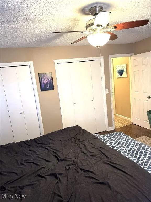 Bedroom with a textured ceiling, two closets, and a ceiling fan