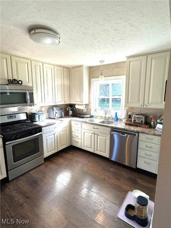 Kitchen featuring appliances with stainless steel finishes, a textured ceiling, dark wood-style floors, pendant lighting, and light stone counters