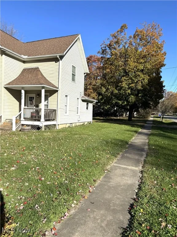 View of side of property with a lawn, roof with shingles, and covered porch