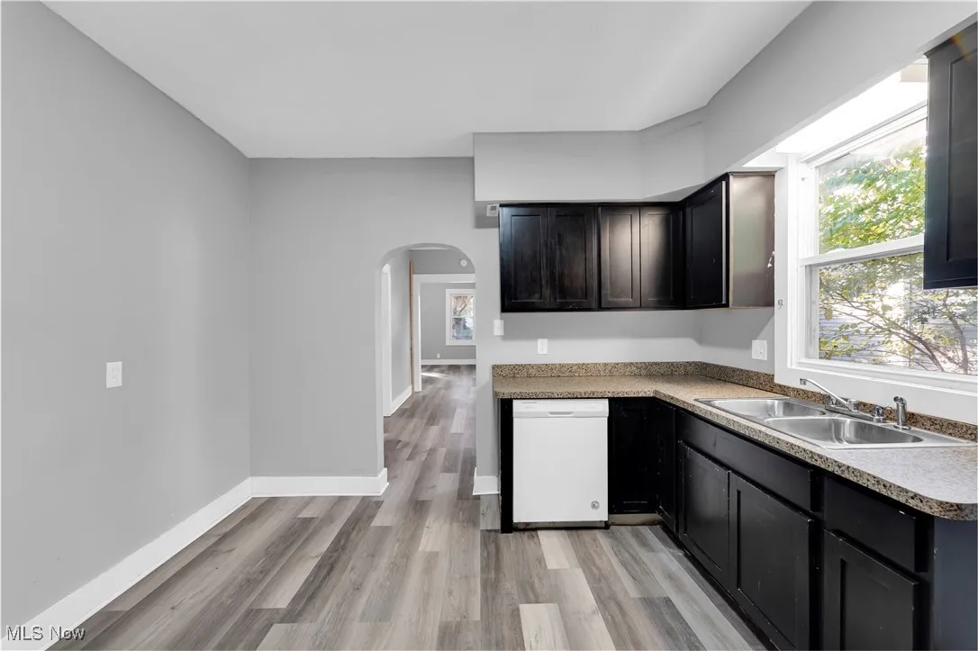 Kitchen with arched walkways, dishwasher, light wood finished floors, and dark cabinetry