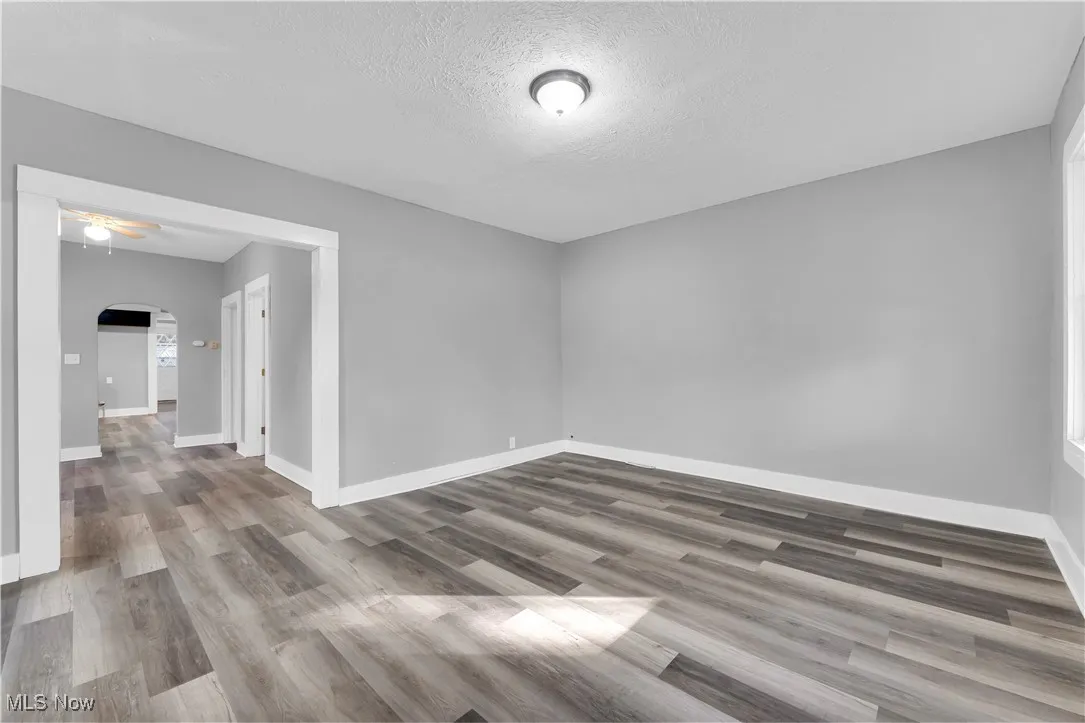 Unfurnished room with arched walkways, a textured ceiling, and light wood finished floors