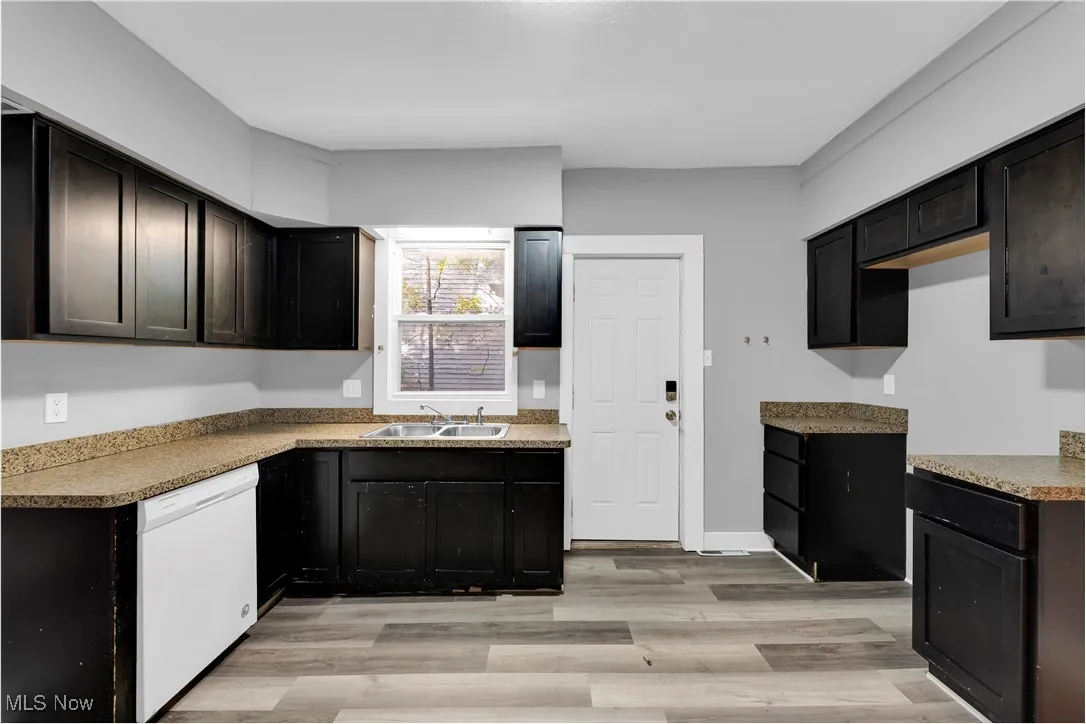 Kitchen featuring white dishwasher, light wood-style floors, light countertops, and dark cabinetry