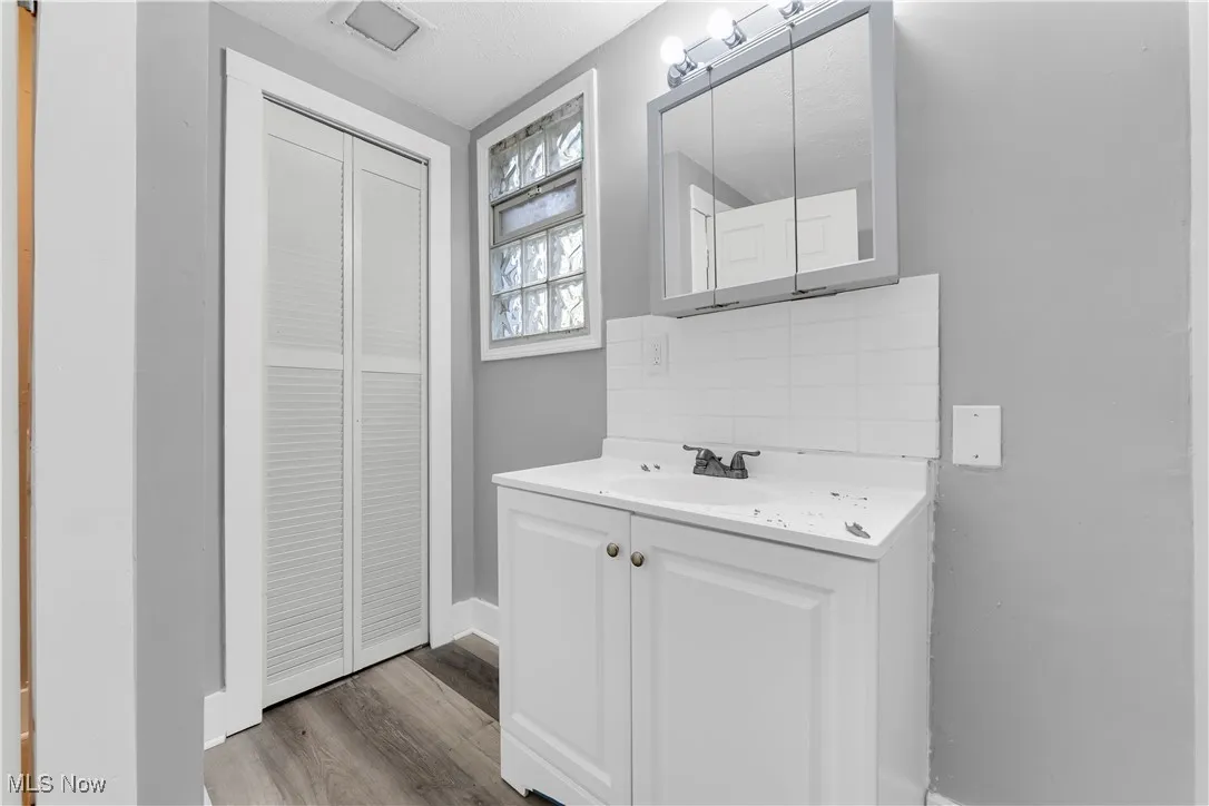 Bathroom with a closet, backsplash, vanity, and dark wood-style flooring