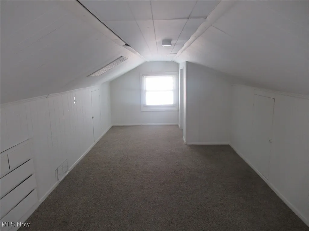 Additional living space with carpet flooring, vaulted ceiling, and wooden walls