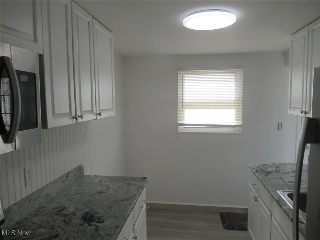 Kitchen featuring light wood-style floors, stainless steel microwave, white cabinets, light stone countertops, and freestanding refrigerator
