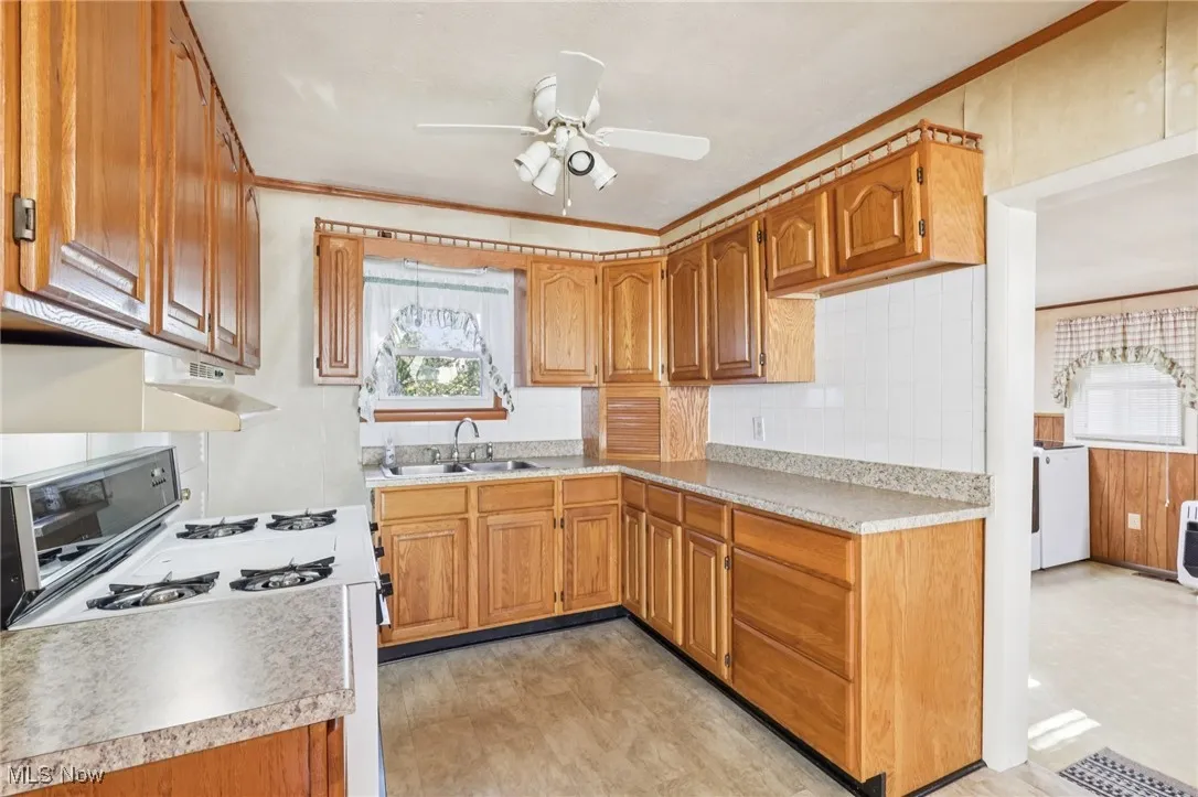 Kitchen with brown cabinetry, crown molding, gas range gas stove, tasteful backsplash, and light countertops
