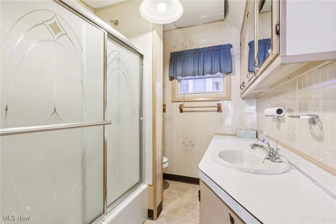 Bathroom featuring vanity, light tile patterned flooring, tile walls, and combined bath / shower with glass door