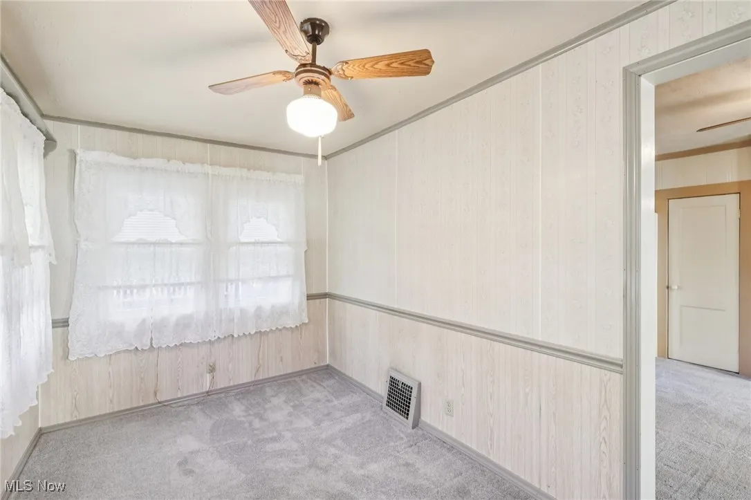 Empty room featuring ceiling fan, light colored carpet, crown molding, and wallpapered walls