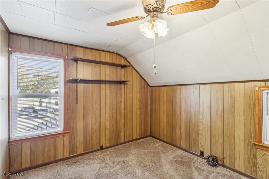 Additional living space featuring wood walls, vaulted ceiling, light colored carpet, and ceiling fan