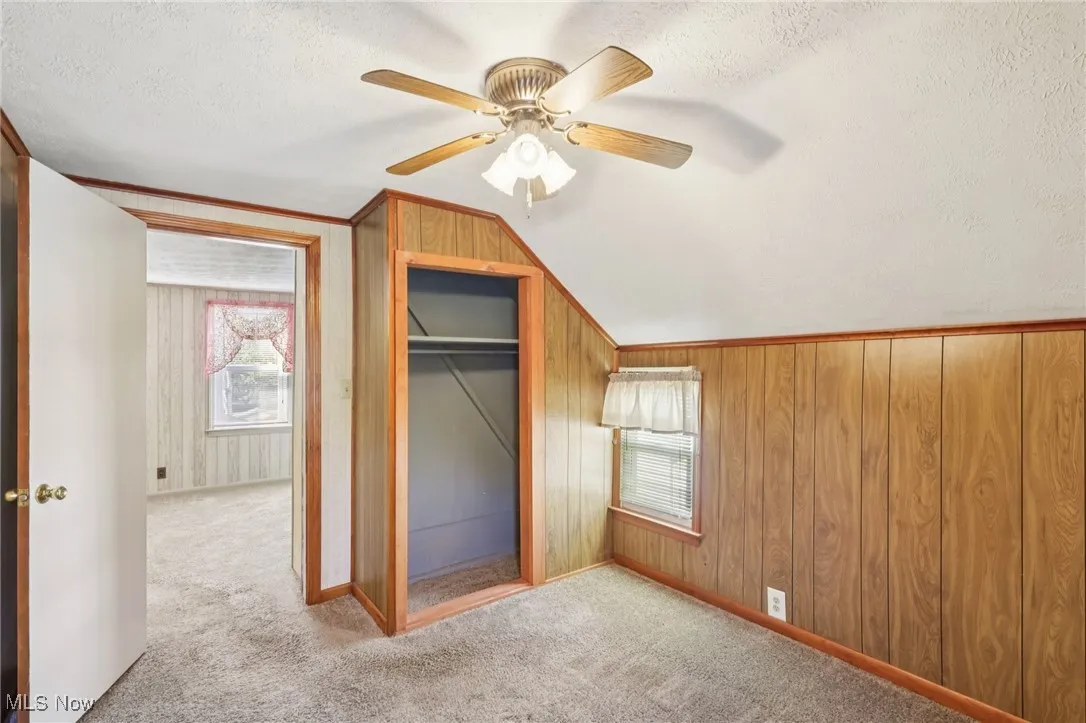 Unfurnished bedroom with a textured ceiling, carpet flooring, lofted ceiling, wood walls, and ceiling fan