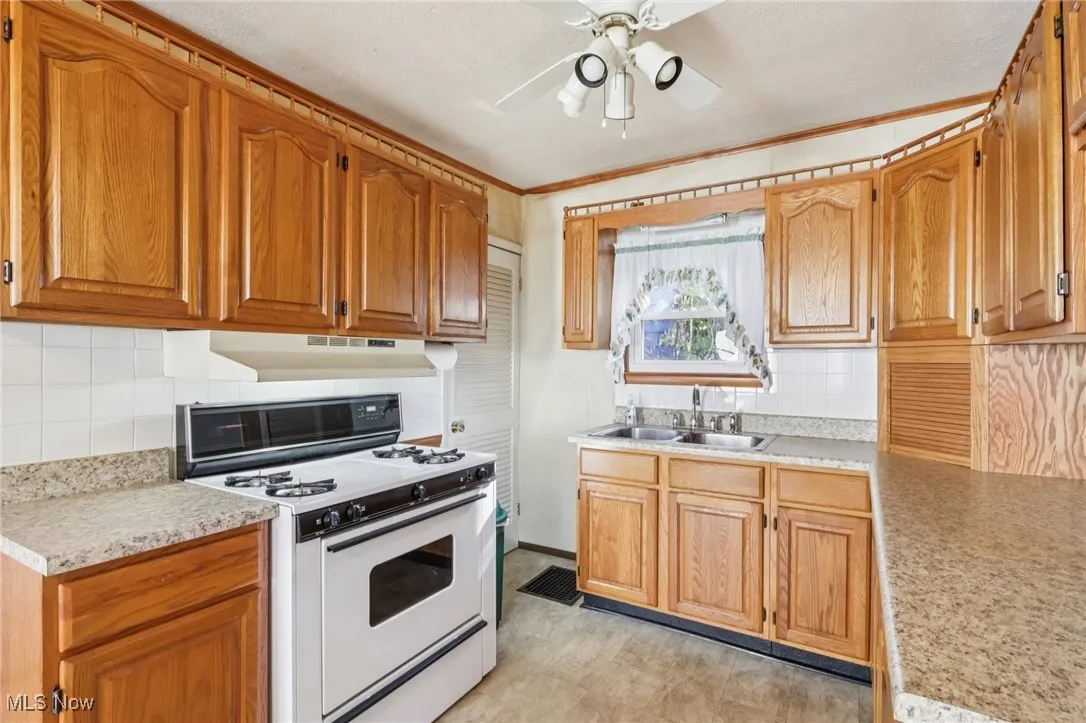 Kitchen featuring white gas range oven, tasteful backsplash, light countertops, brown cabinets, and ornamental molding