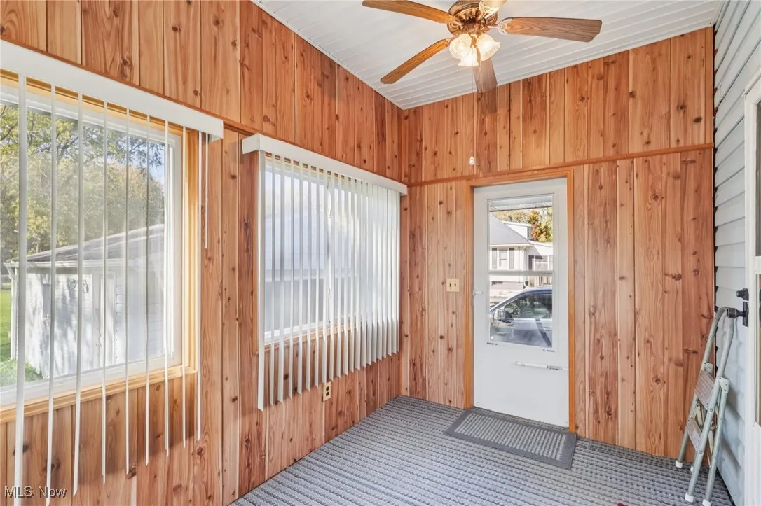Doorway with carpet, wood walls, and a ceiling fan