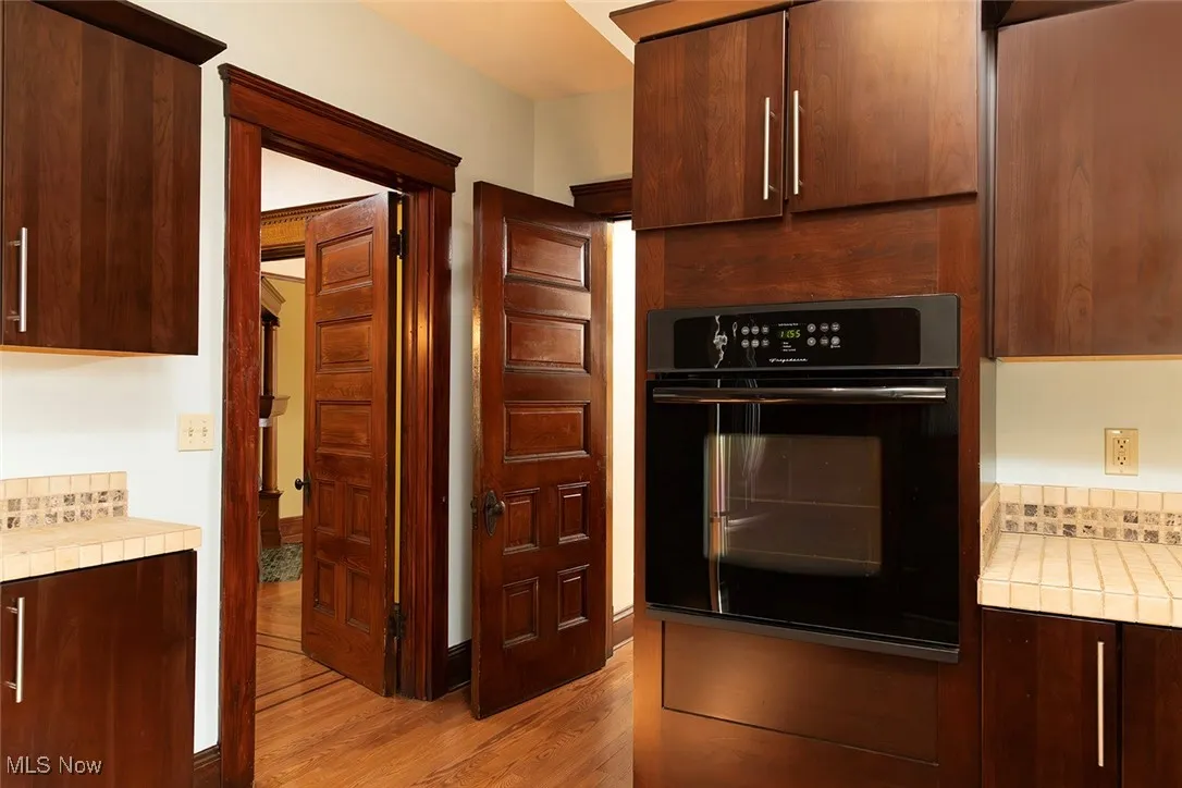 Kitchen featuring tile counters, oven, dark brown wood cabinetry, and light wood flooring